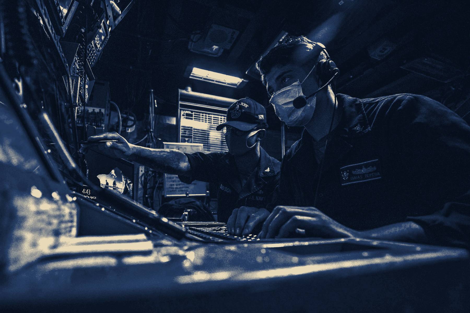 Sailors at consoles in a darkened compartment